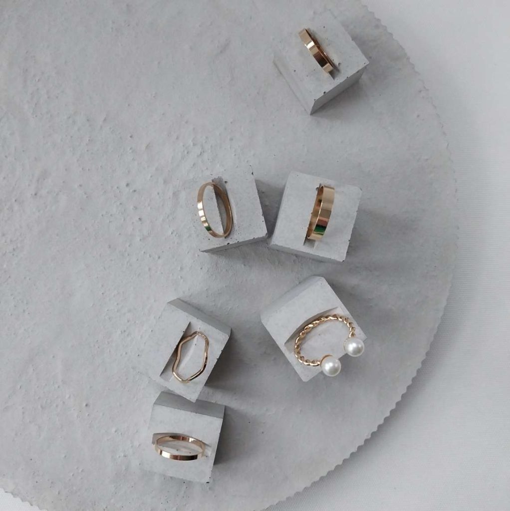 Ein graues Betontablett bildet den Hintergrund und die Würfel Ringständer von PasingaProps präsentieren den Schmuck [auch hier Kostümschmuck der Betonung findet]