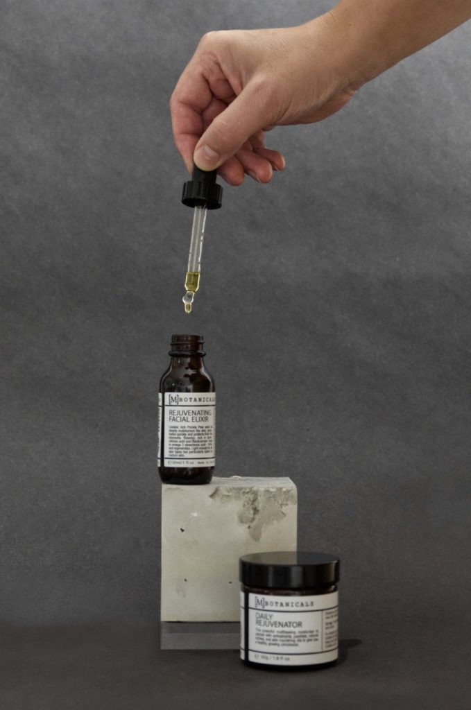 Heller Beton Würfel präsentiert Kosmetik Produkte mit Hand die Öl gefüllte Pipette hält über der Flasche auf dem Würfel
